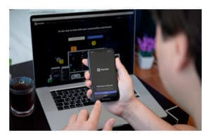 Aplicación Discord - joven tomando celular con el programa abierto y una laptop de fondo